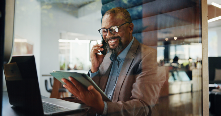 Man on phone observing ipad at desk